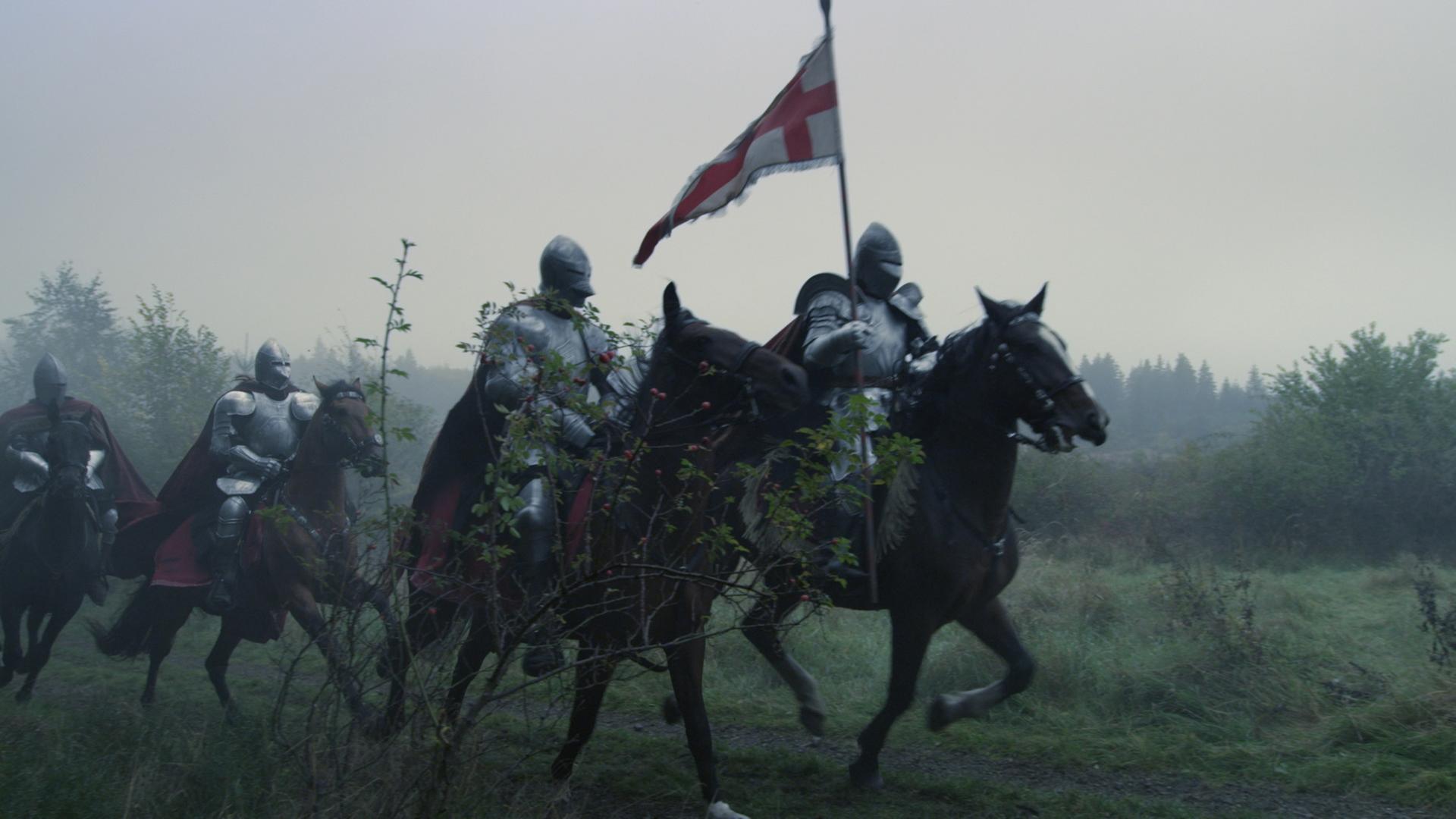 Mehrere gerüstete Ritter reiten über eine Wiese, der vorderste hält eine Fahne.
