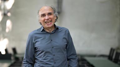 Porträtfoto eines Mannes mit kurzen lockigen graumelierten Haaren, Halbglatze und Brille.