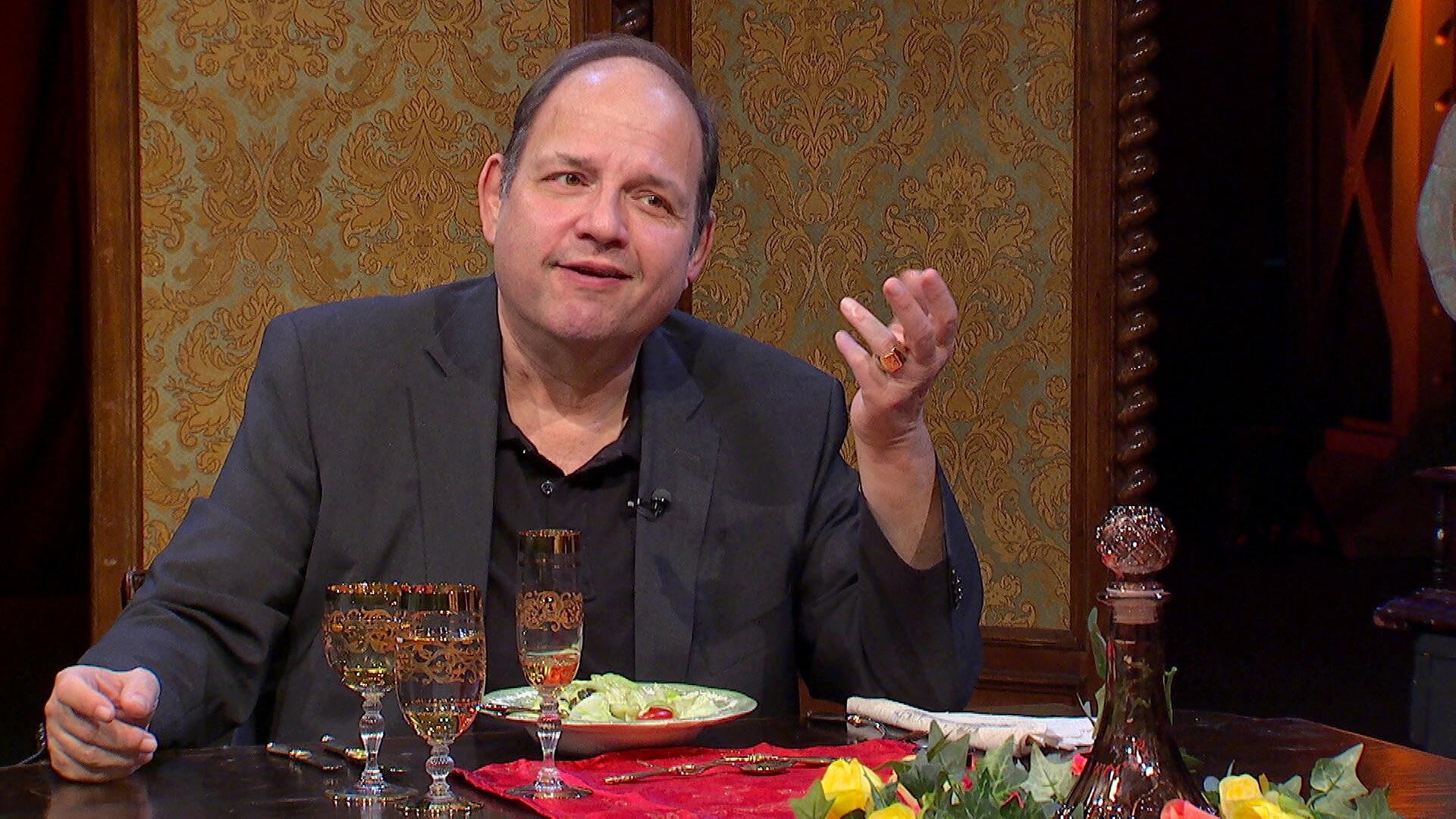 Gerald Pichowetz sitzt bei der Impro-Comedy-Show „Dinner für Zwei“ am Esstisch.  