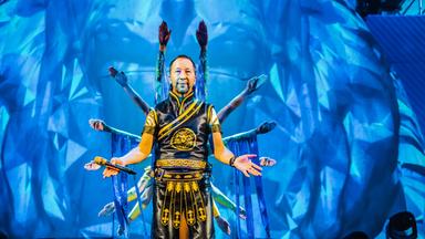 DJ Bobo vor einem blauen Bühnenbild, hinter ihm Tänzer.