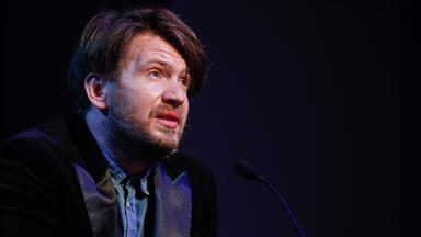 Porträtfoto eines Mannes mit Kinnbart vor dunklem Hintergrund