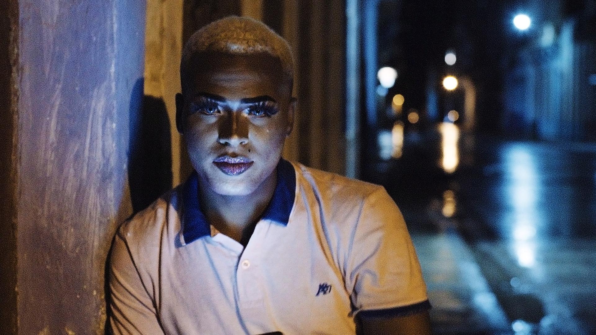 Portraitbild eines schönen jungen Mannes mit kurzrasierten, blond gefärbten Haaren und geschminktem Gesicht.