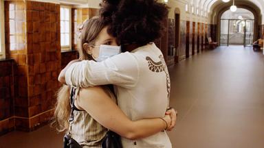 Zwei Personen stehen auf einem langen Flur und umarmen sich.