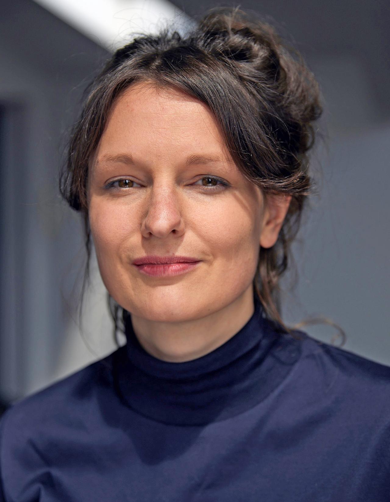 Porträtfoto von Nele Dehnenkamp, die einen dunkelblauen Rollkragenpullover trägt und in die Kamera lächelt.