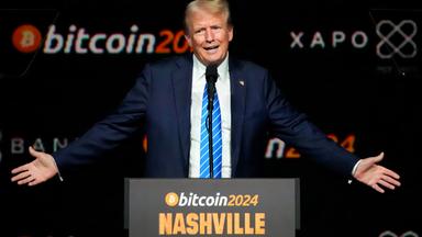 Donald Trump - ein älterer Mann mit graublonden Haaren und im Anzug redet gestikulierend an einem Rednerpodest, auf dem bitcoin 2024 Nashville steht.