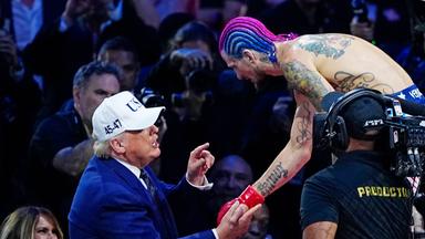 US-Präsident Donald Trump, ein älterer Mann mit Baseball-Kappe und im dunkelblauen Anzug gibt einem MMA-Kämpfer mit nacktem tätowierten Oberkörper und gefärbten Haaren die Hand, während er mit dem Finger auf ihn zeigt und redet.