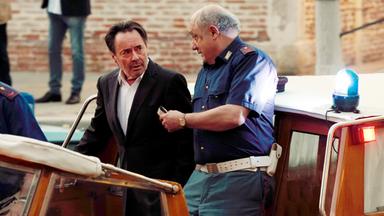 Ein Mann im dunklen Anzug und ein Mann in Polizeiuniform stehen auf einem Boot und unterhalten sich