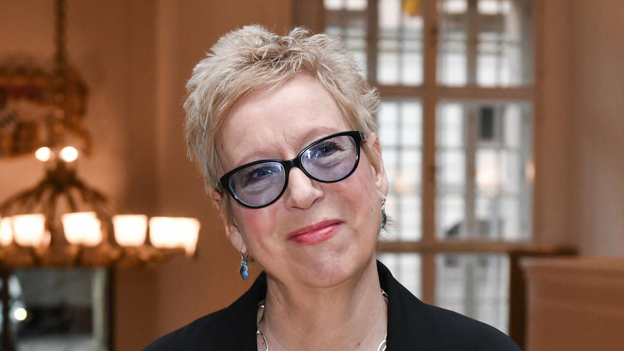 Eine Frau mit kurzen blonden Haaren und dunkler Brille lächelt in die Kamera.