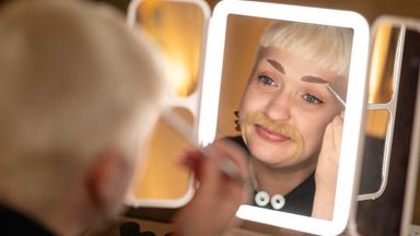 Anas schminkt sich in beleuchtetem Spiegel.