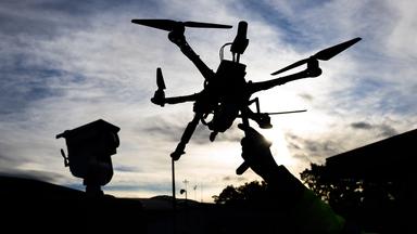 Der dunkle Umriss einer Drohne, die von einer Hand vor einen bewölkten Himmel hochgehalten wird.