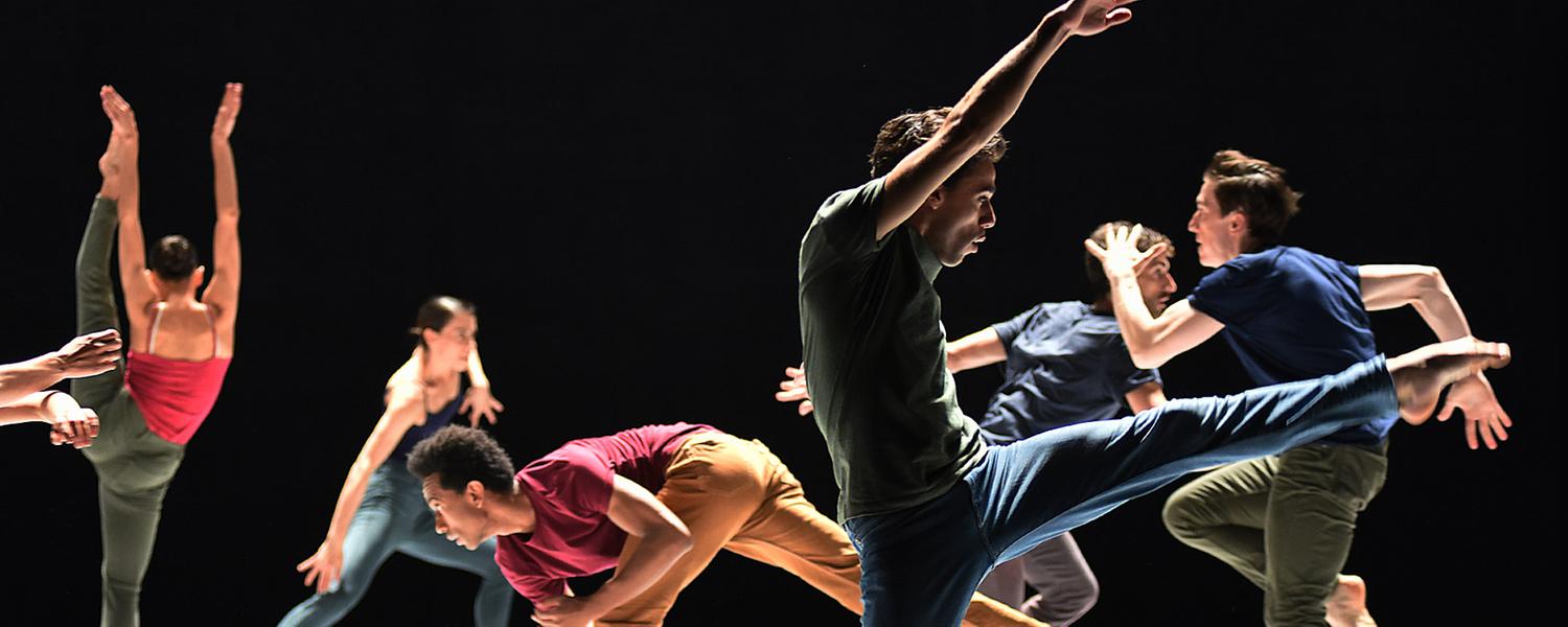 Tänzer in verschiedener Kleidung vor einem schwarzen Hintergrund. 