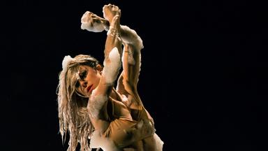 Tänzerin Garazi Perez Oloriz steht in einer mit Schaum gefüllten Plastikwanne, mal den Kopf nach vorne geneigt, mal die Hände nach oben gestreckt. Dabei bedeckt der Schaum teilweise ihren Körper.