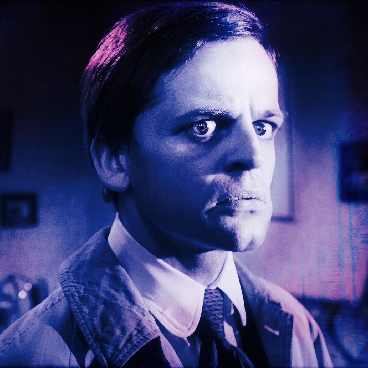 Zwei Männer in einem Raum  einer blickt kritisch auf den anderen, der mit erschrockenem Gesichtsausdruck zur Seite schaut.