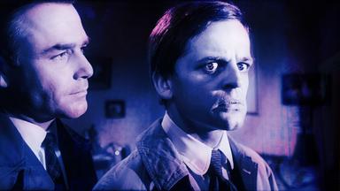 Zwei Männer in einem Raum  einer blickt kritisch auf den anderen, der mit erschrockenem Gesichtsausdruck zur Seite schaut.