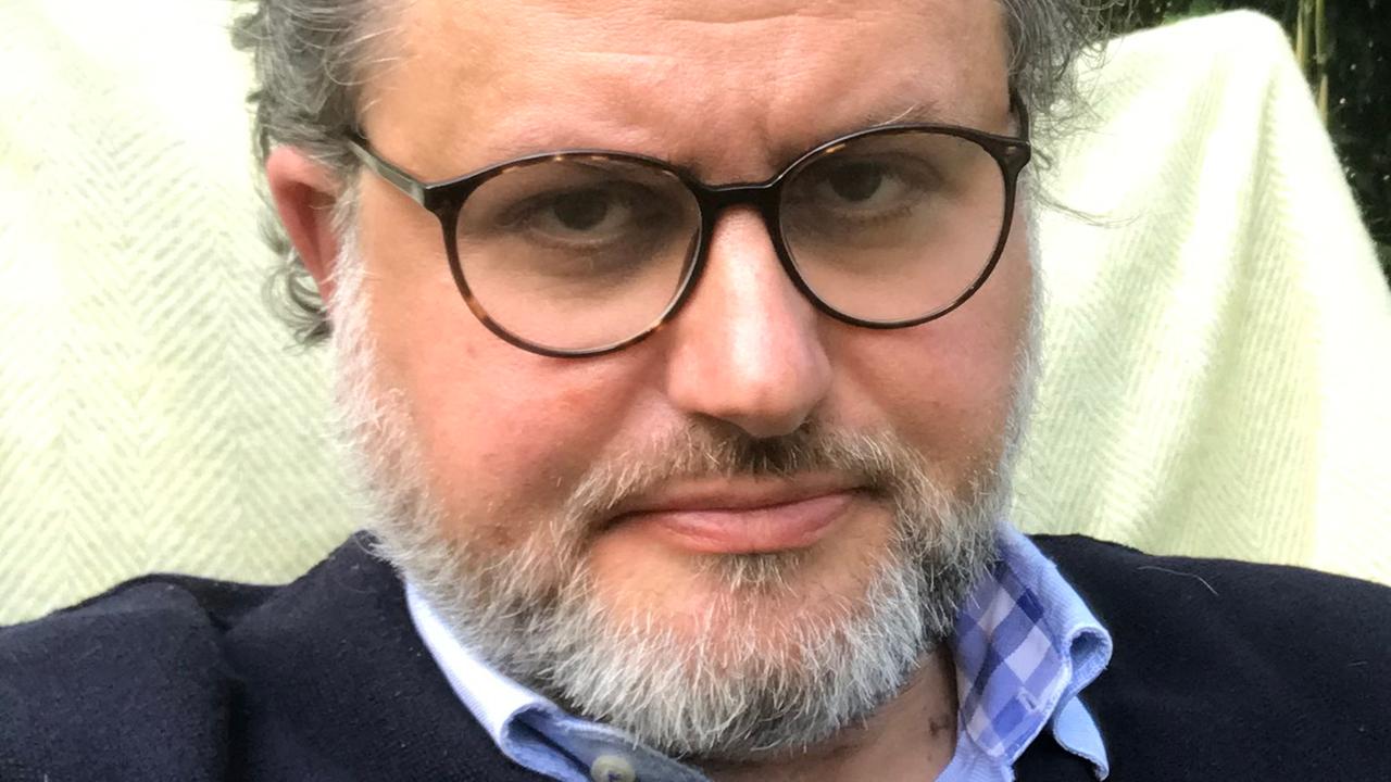 Mann mit zurückgekämmtem graumeliertem Haar, Bart und Brille.