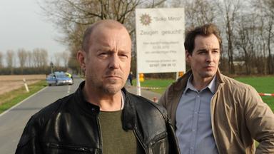 Ingo Thiel (Heino Ferch) und Mario Eckartz (Felix Kramer) auf einer gesperrten Landstraße vor einem Schild, das Zeugen aufruft, sich zu melden.