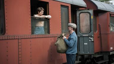 Sonja (Ida Engvoll) steht im Zug am offenen Fenster und lächelt Ove (Filip Berg) an, der einen Seesack trägt und mit ihr spricht.
