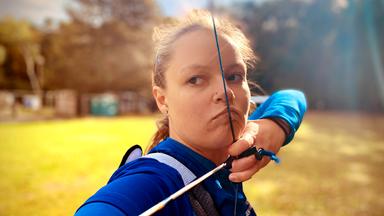 Frau spannt die Sehne ihres Bogens über Nase und Mund