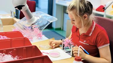 Eine Frau fertigt rosafarbene Sterne in der Sternemanufaktur an.