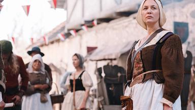 Spielszene: Hebamme Anna Stein (Julia Thurnau)  steht auf der Straße zwischen anderen Menschen