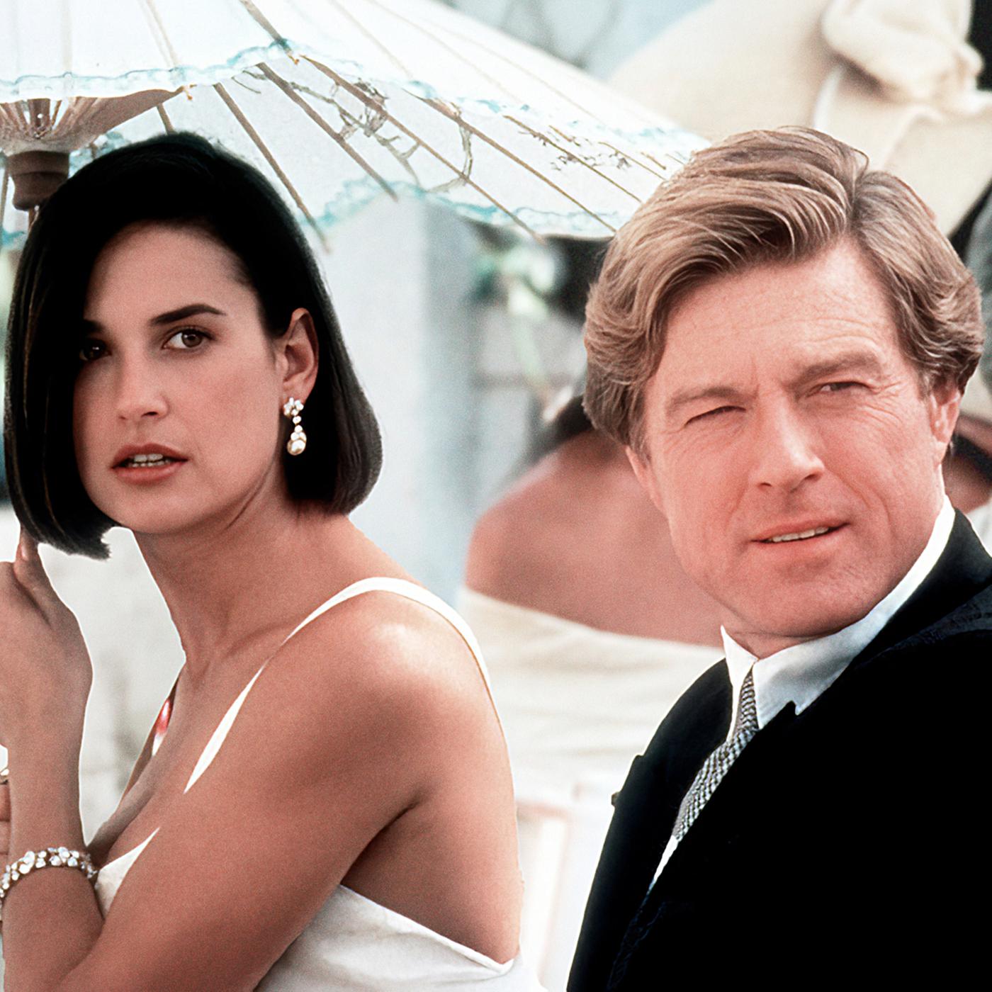 Eine dunkelhaarige Frau (Demi Moore) mit einem Sonnenschirm in der Hand mit einem blonden Mann (Robert Redford) an ihrer Seite