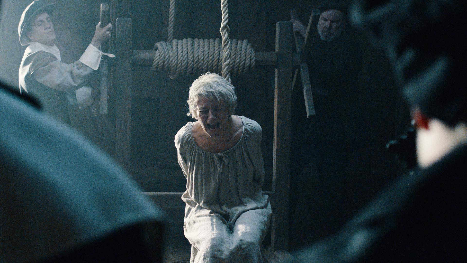 Spielszene: Vermeintliche Hexe schreit. Sie wird von zwei Männern gehängt