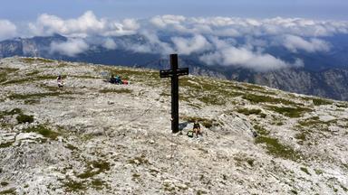 Ein Großes Kreuz auf einem Berg mit Blick auf andere Berge in einer blauen Wolkendecke