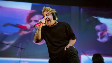 Electric Callboy-Sänger Nico Sallach ist auf der Bühne und singt in ein rosa Mikrofon.