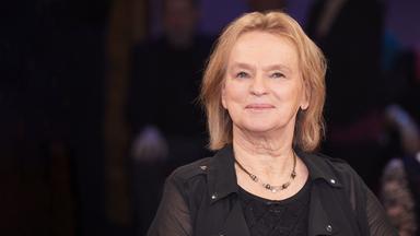 Eine ältere Frau mit hellen, schulterlangen Haaren, blilckt lächelnd in die Kamera.