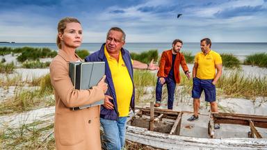 "Ella Schön - Die nackte Wahrheit": Ella steht mit ihrem Klienten Holger Packebusch (Hilmar Eichhorn) am Strand. Hinter ihnen unterhalten sich seine Söhne Maik (Stefan Rudolf) und Kurt (Christoph Letkowski).