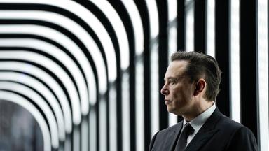 Ein Mann mittleren Alters im grauen Anzug steht vor einem schwarz-weiß-gestreiften Hintergrund.