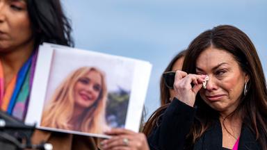 Eine Frau mit langen dunklen Haaren wischt sich mit einem Taschentuch die Tränen aus den Augen, während eine zweite das Foto einer jungen blonden Frau hoch hält.