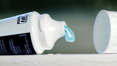 Türkisfarbene Zahnpasta läuft aus einer weissen Tube