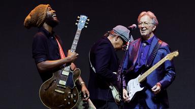 Eric Clapton steht mit seiner Gitarre und einem weiteren Musiker mit Gitarre auf der Bühne.