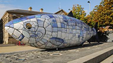 Eine große Fischskulptur aus blauen und weißen Kacheln vor einem Gebäude.