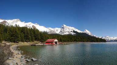 Ein Bootshaus an einem kanadischen See. Im Hintergrund schneebedeckte Berge.