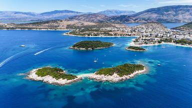 Kleine Inseln und Boote im blauen Wasser vor einer hügeligen Küste im Hintergrund