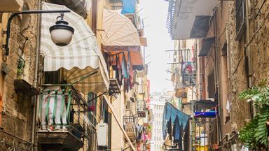 Eine enge Gasse zwischen Häuserreihen. Kleine Balkone und trocknende Wäschen darauf. 