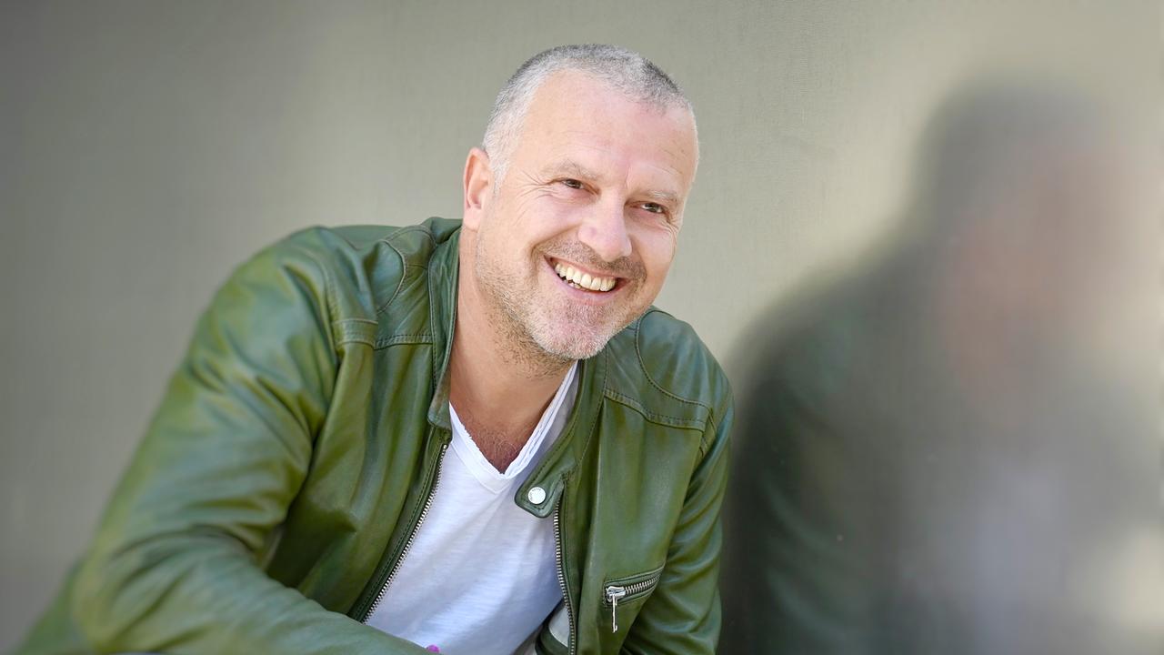  Ein Mann, mit kurzen Haaren, lacht und guckt an der Kamera vorbei