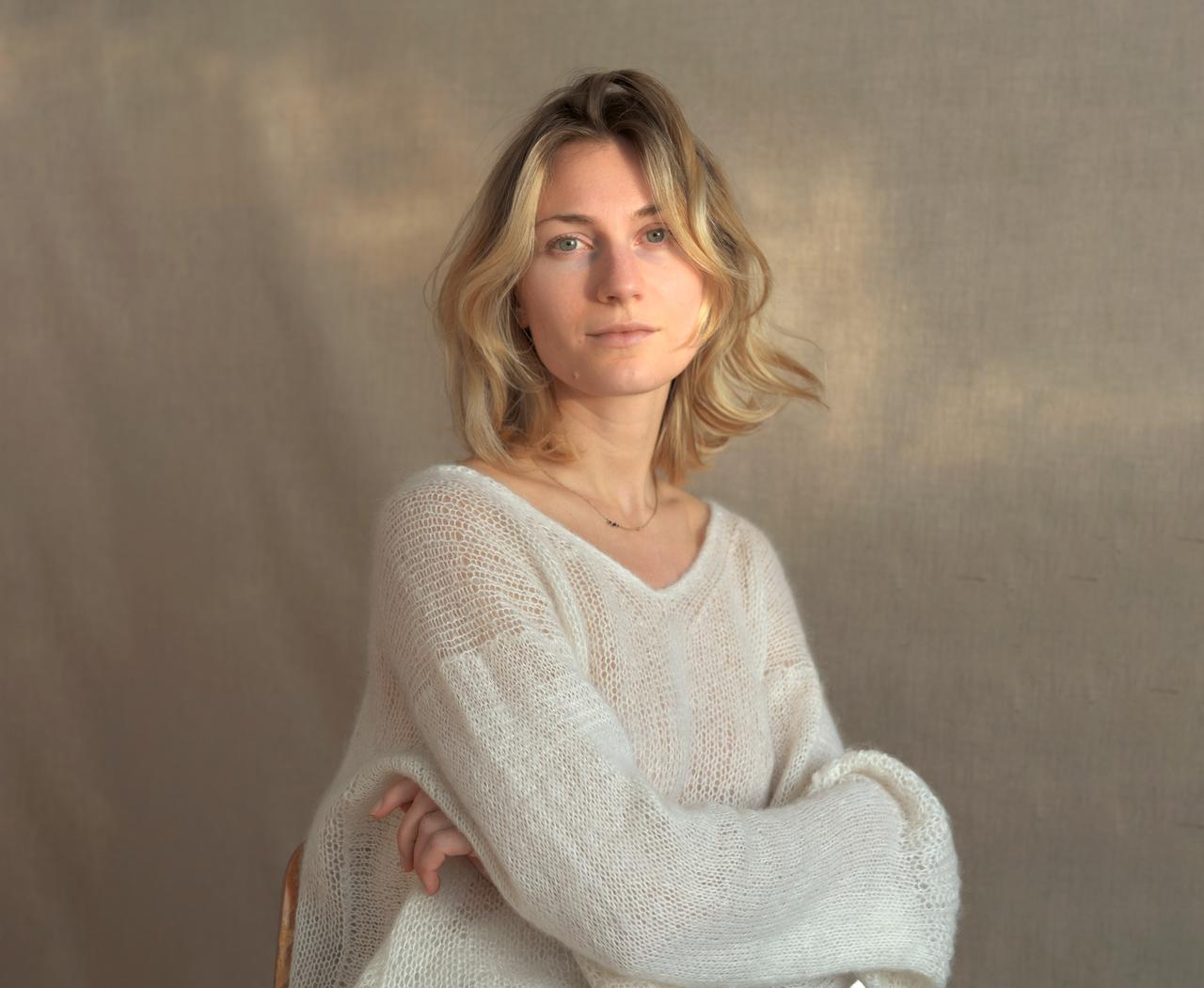 Eine Frau in einem hellen Pulli vor einer beigefarbenen Wand