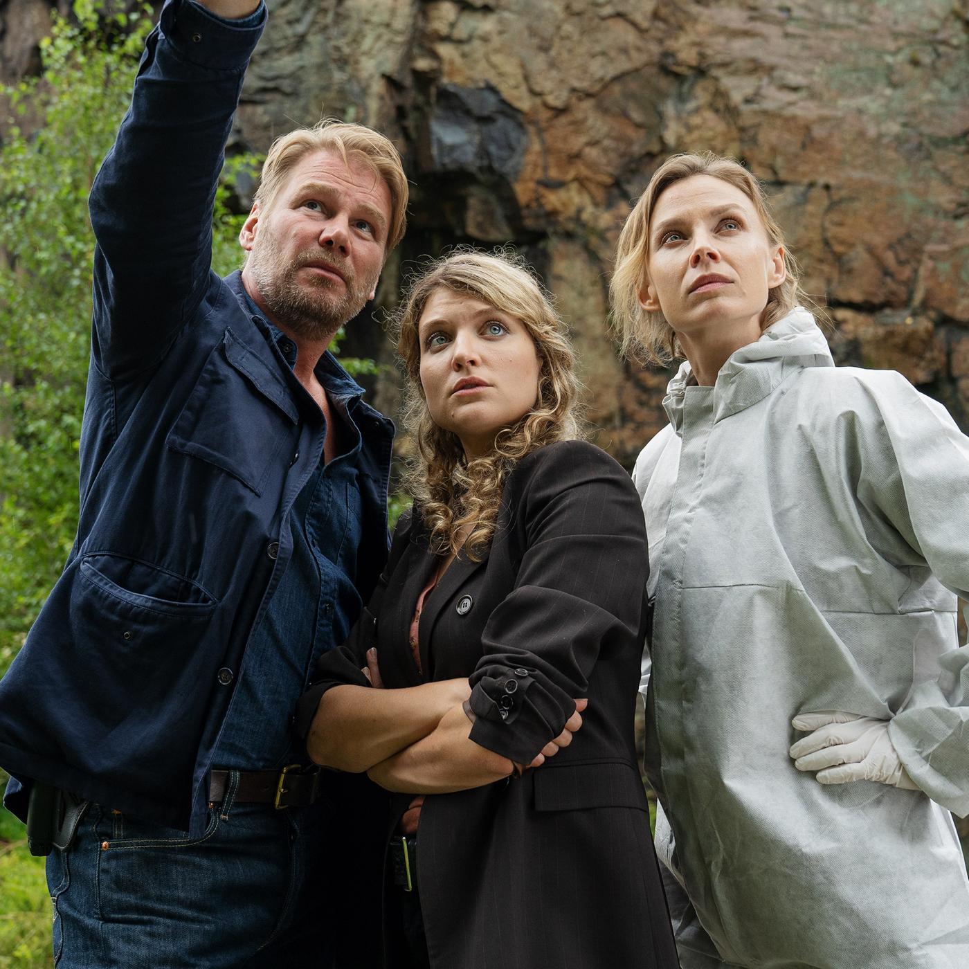 Vor einer Felswand stehend zeigt Kommissar Winkler (Kai Scheve) Kommissarin Karina Szabo (Lara Mandoki) und Pathologin Dr. Elena Kulikova (Masha Tokareva) die Absturzstelle.