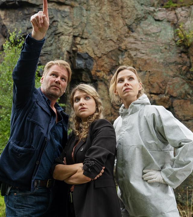 Vor einer Felswand stehend zeigt Kommissar Winkler (Kai Scheve) Kommissarin Karina Szabo (Lara Mandoki) und Pathologin Dr. Elena Kulikova (Masha Tokareva) die Absturzstelle.