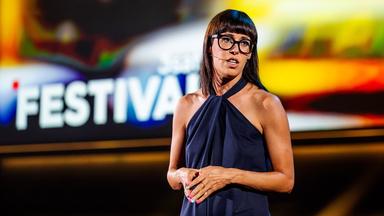 Eva Karl Faltermeier steht in der Mitte des Bildes. Sie faltet die Hände vor ihrem Bauch. Die Bühne im Hintergrund ist gelb beleuchtet. 