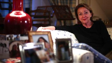 Eine Frau sitzt auf einer Couch, im Vordergrund stehen Bilder.