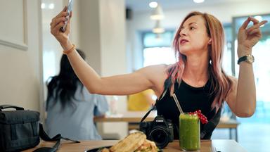 Eine Frau in einem schwarzen Kleid filmt sich mit ihrem Handy.