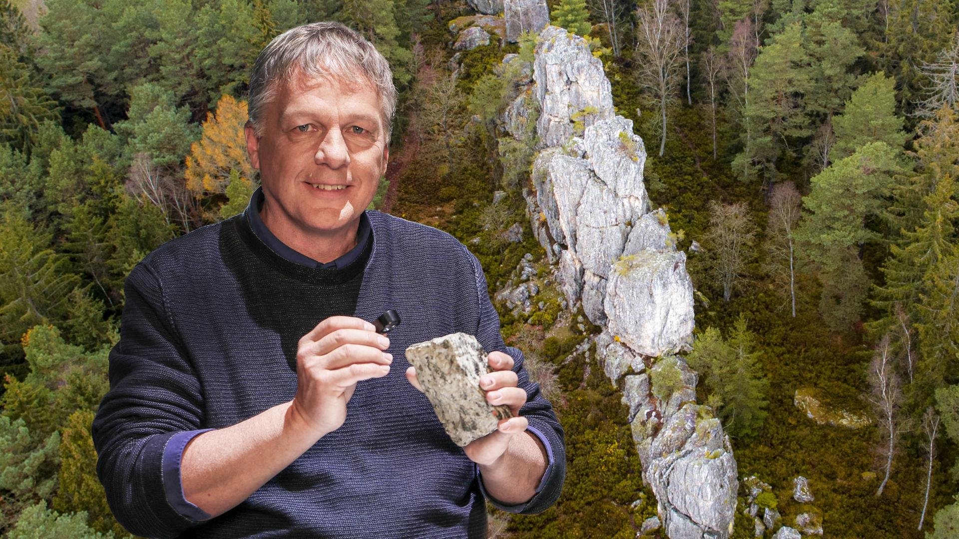 Ein Mann im Pullover hält lächelnd einen grauen Stein. Eine Steinlandschaft ist im Hintergrund.