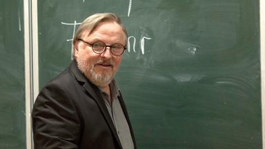 "Extraklasse": Ralph Friesner (Axel Prahl) steht seitlich zu einer Schultafel, sein Blick ist in den Raum gerichtet. Auf der Tafel steht sein Name.