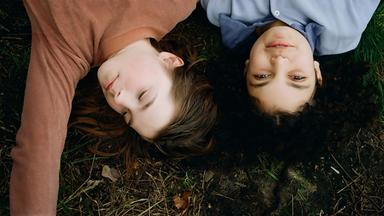 Zwei junge Mädchen liegen nebeneinander im Gras.