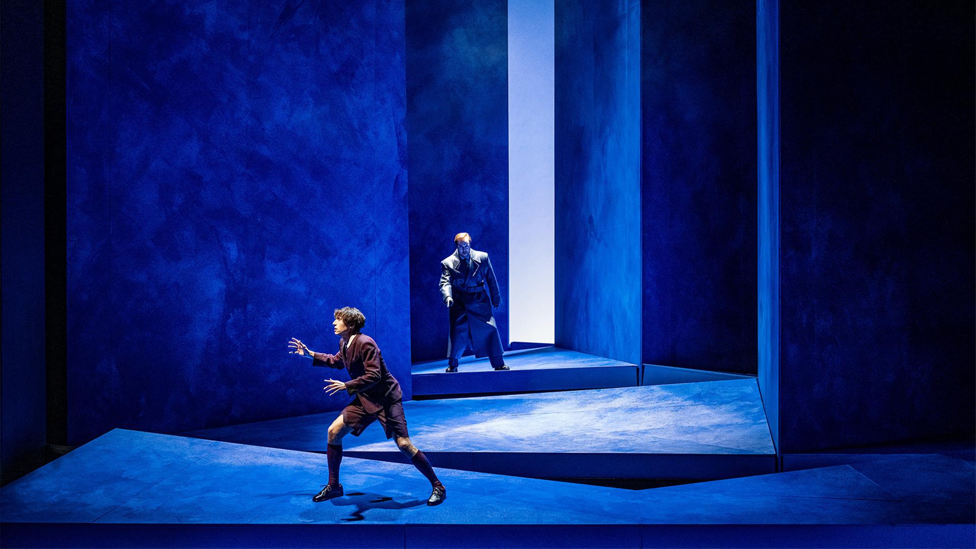 Auf einer blauen Bühne stehen zwei Männer hintereinander.