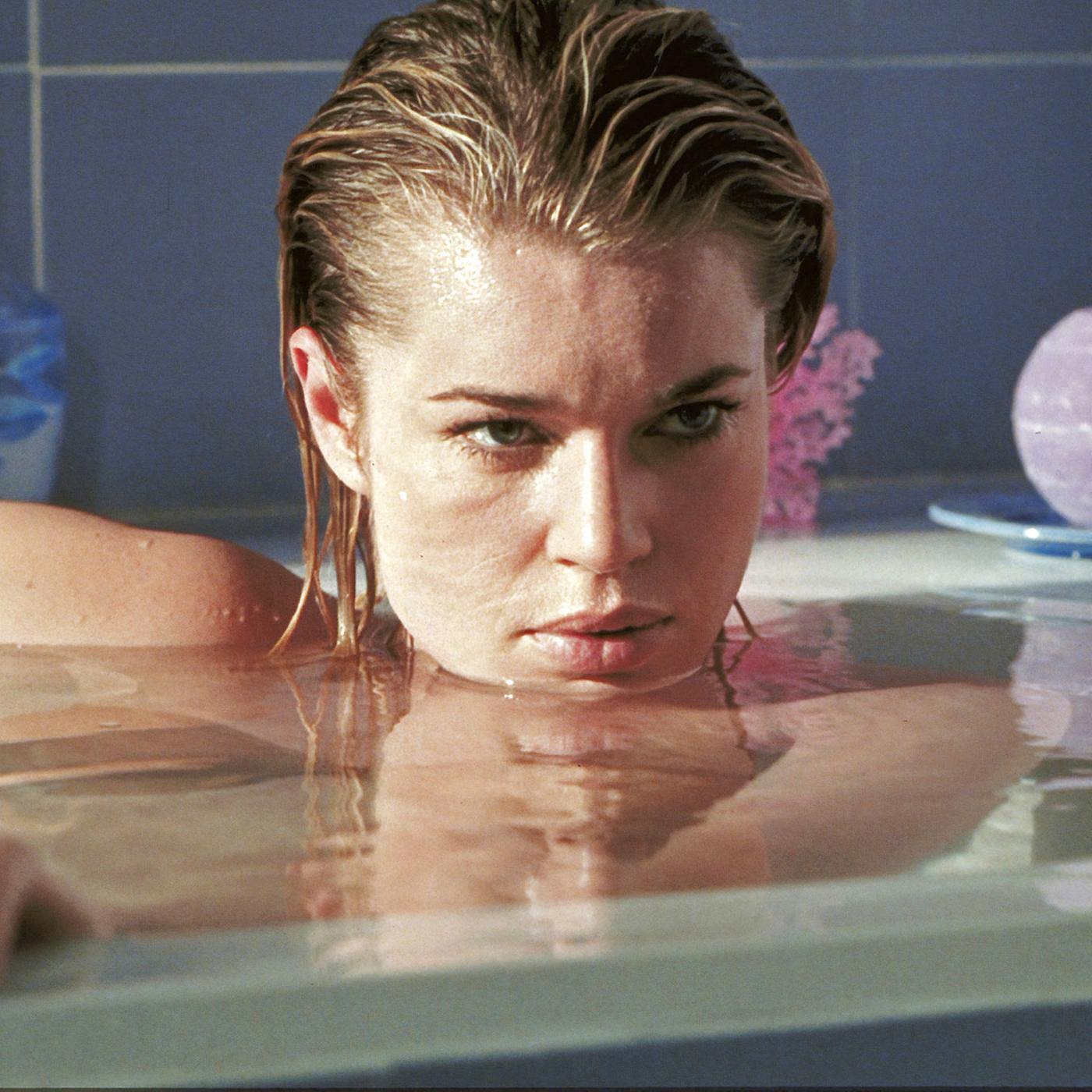 Femme Fatale: Laure (Rebecca Romijn) liegt in einer vollen Badewanne, ihr Gesicht knapp über der Wasseroberfläche, und blickt geheimnisvoll zur Seite.